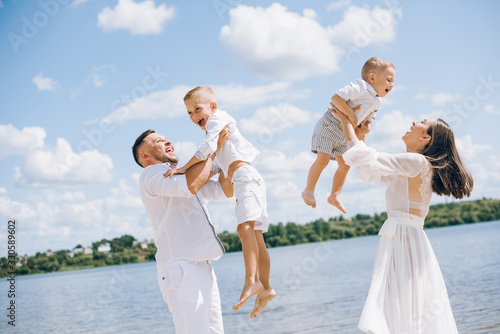 Young family with kids in white clothes walking on the sandy beach, they have fun.