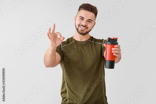 Sporty man with protein shake showing OK on light background
