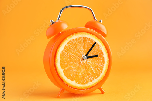 Creative alarm clock with citrus fruit on color background
