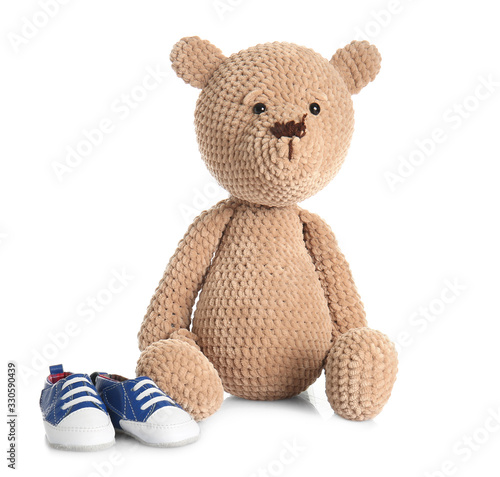 Teddy bear with baby shoes on white background