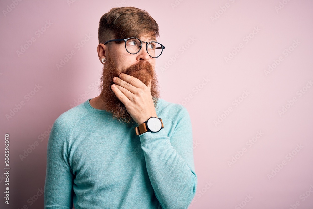 Handsome Irish redhead man with beard wearing glasses over pink isolated background with hand on chin thinking about question, pensive expression. Smiling with thoughtful face. Doubt concept. Handsome Irish redhead man with beard wearing glasses over pink isolated background with hand on chin thinking about question, pensive expression. Smiling with thoughtful face. Doubt concept.