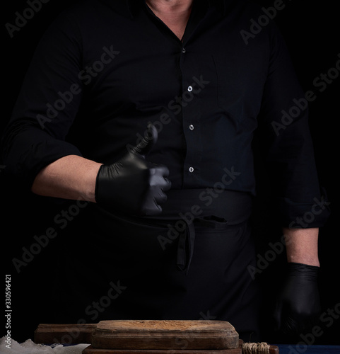 male cook in black uniform and black latex gloves shows like approval gesture