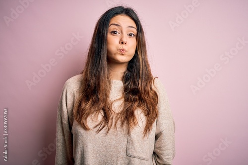 Εκτύπωση καμβά Young beautiful brunette woman wearing casual sweater standing over pink background puffing cheeks with funny face