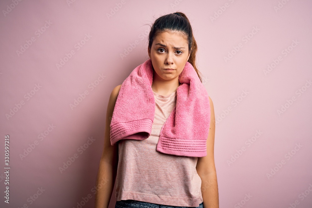 Young beautiful brunette sportswoman wearing sportswear and towel over pink background skeptic and nervous, frowning upset because of problem. Negative person. Young beautiful brunette sportswoman wearing sportswear and towel over pink background skeptic and nervous, frowning upset because of problem. Negative person.