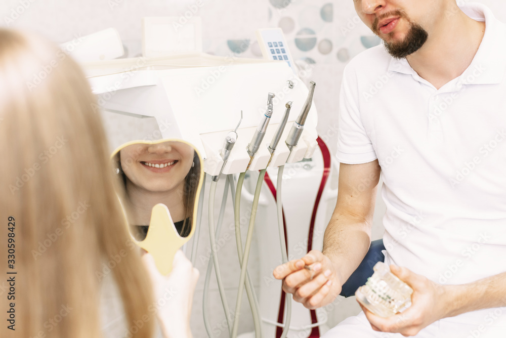 A woman, a dentistry client, sits in a dental chair and looks at her smile in the mirror. The result of dental work is a happy healthy smile A woman, a dentistry client, sits in a dental chair and looks at her smile in the mirror. The result of dental work is a happy healthy smile