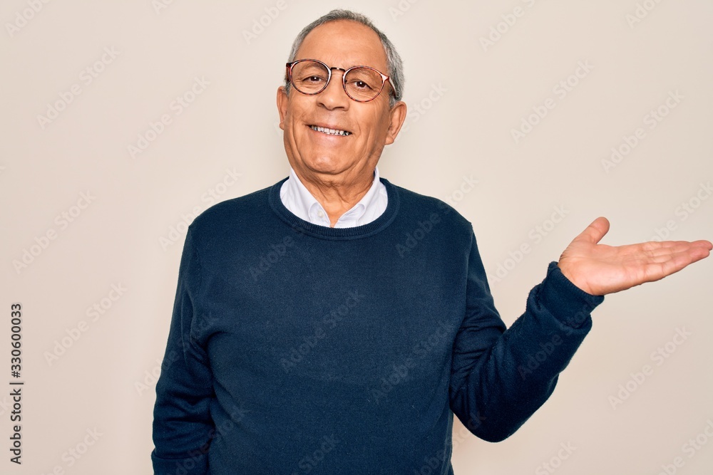 Naklejka premium Senior handsome grey-haired man wearing sweater and glasses over isolated white background smiling cheerful presenting and pointing with palm of hand looking at the camera.