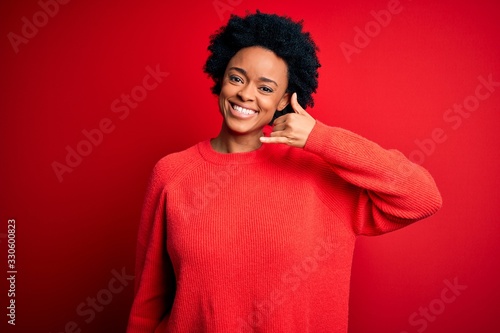 Young beautiful African American afro woman with curly hair wearing casual sweater smiling doing phone gesture with hand and fingers like talking on the telephone. Communicating concepts.