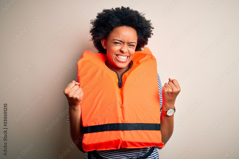Young African American afro woman with curly hair wearing orange protection lifejacket very happy and excited doing winner gesture with arms raised, smiling and screaming for success. Celebration Young African American afro woman with curly hair wearing orange protection lifejacket very happy and excited doing winner gesture with arms raised, smiling and screaming for success. Celebration