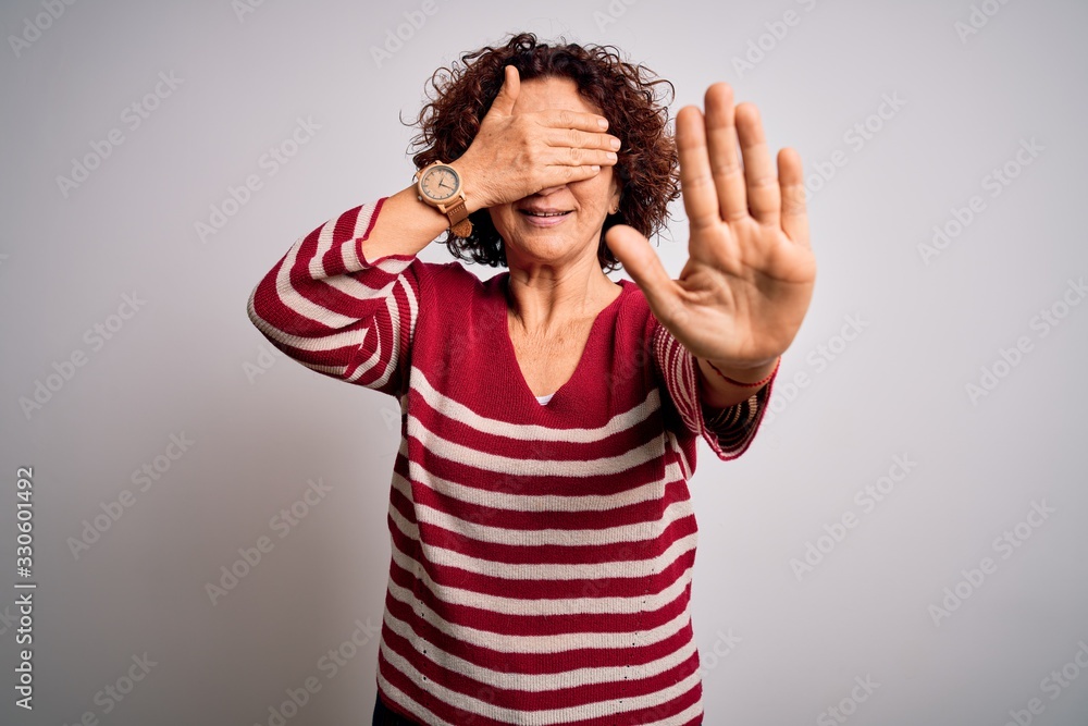 Middle age beautiful curly hair woman wearing casual striped sweater over white background covering eyes with hands and doing stop gesture with sad and fear expression. Embarrassed and negative Middle age beautiful curly hair woman wearing casual striped sweater over white background covering eyes with hands and doing stop gesture with sad and fear expression. Embarrassed and negative