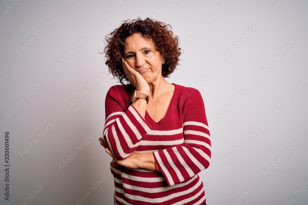 Middle age beautiful curly hair woman wearing casual striped sweater over white background thinking looking tired and bored with depression problems with crossed arms. Middle age beautiful curly hair woman wearing casual striped sweater over white background thinking looking tired and bored with depression problems with crossed arms.