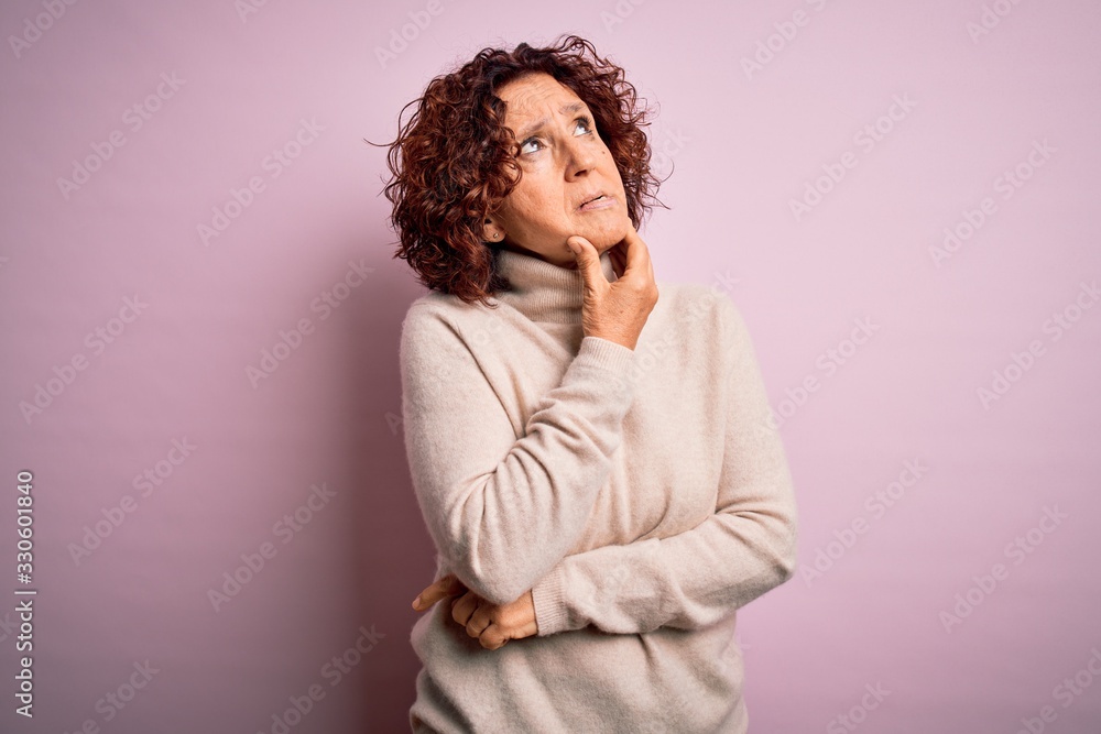 Middle age beautiful curly hair woman wearing casual turtleneck sweater over pink background Thinking worried about a question, concerned and nervous with hand on chin