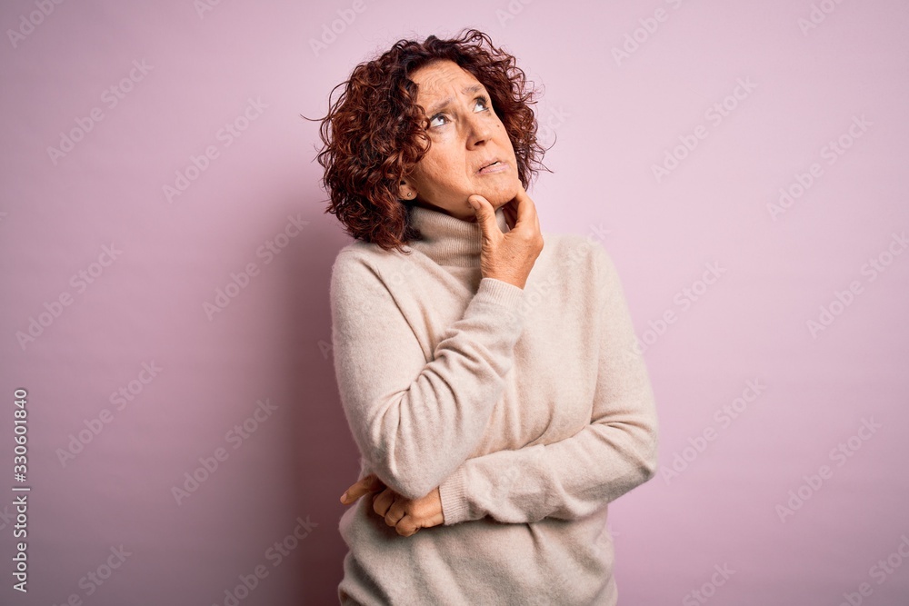 Middle age beautiful curly hair woman wearing casual turtleneck sweater over pink background Thinking worried about a question, concerned and nervous with hand on chin Middle age beautiful curly hair woman wearing casual turtleneck sweater over pink background Thinking worried about a question, concerned and nervous with hand on chin