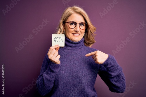 Photos Middle age beautiful blonde woman wearing glasses holding reminder paper with ye