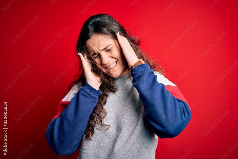 Young beautiful woman with curly hair wearing casual sweatshirt over isolated red background with hand on headache because stress. Suffering migraine. Young beautiful woman with curly hair wearing casual sweatshirt over isolated red background with hand on headache because stress. Suffering migraine.