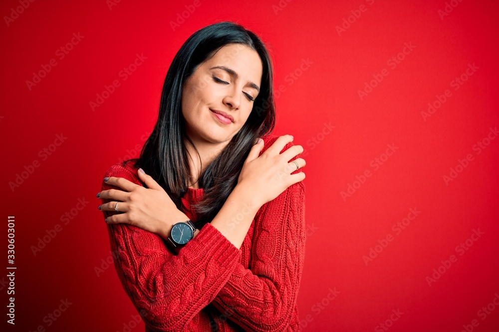 Young brunette woman with blue eyes wearing casual sweater over isolated red background Hugging oneself happy and positive, smiling confident. Self love and self care Young brunette woman with blue eyes wearing casual sweater over isolated red background Hugging oneself happy and positive, smiling confident. Self love and self care