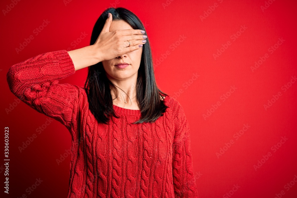 Young brunette woman with blue eyes wearing casual sweater over isolated red background covering eyes with hand, looking serious and sad. Sightless, hiding and rejection concept Young brunette woman with blue eyes wearing casual sweater over isolated red background covering eyes with hand, looking serious and sad. Sightless, hiding and rejection concept