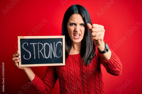 Young brunette woman with blue eyes holding blackboard with strong word message annoyed and frustrated shouting with anger, crazy and yelling with raised hand, anger concept