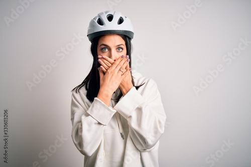 Young cyclist woman with blue eyes wearing bike helmet over isolated white background shocked covering mouth with hands for mistake. Secret concept. © Krakenimages.com