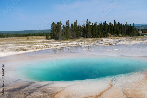 Landscape of blue geyser pool and trees at Yellowstone National Park in Wyoming