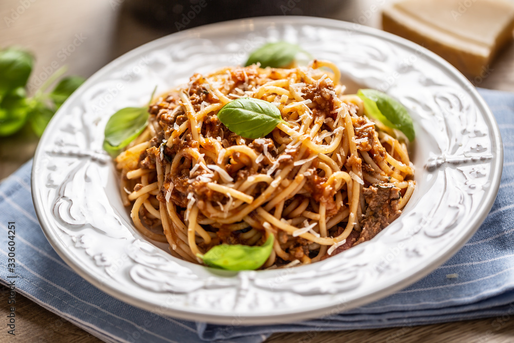 Italian pasta spaghetti bolognese served on white plate with parmesan cheese and basil