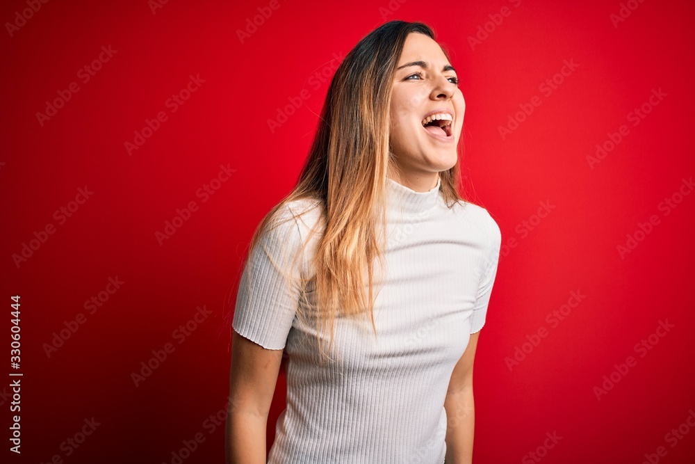 Beautiful blonde woman with blue eyes wearing casual white t-shirt over red background angry and mad screaming frustrated and furious, shouting with anger. Rage and aggressive concept. Beautiful blonde woman with blue eyes wearing casual white t-shirt over red background angry and mad screaming frustrated and furious, shouting with anger. Rage and aggressive concept.