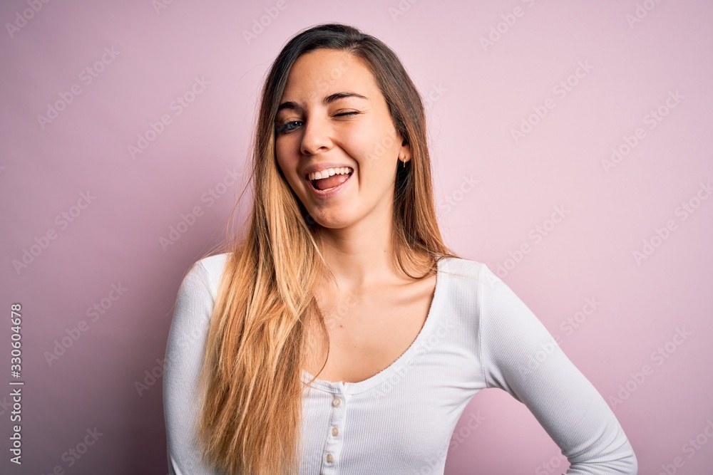 Young beautiful blonde woman with blue eyes wearing white t-shirt over pink background winking looking at the camera with sexy expression, cheerful and happy face. Young beautiful blonde woman with blue eyes wearing white t-shirt over pink background winking looking at the camera with sexy expression, cheerful and happy face.