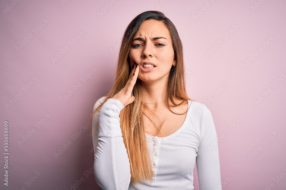 Fototapeta premium Young beautiful blonde woman with blue eyes wearing white t-shirt over pink background touching mouth with hand with painful expression because of toothache or dental illness on teeth. Dentist