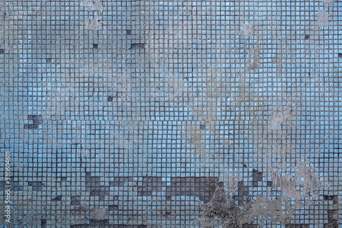old damaged concrete wall with fine blue ceramic tiles and stains of gray cement. rough surface texture
