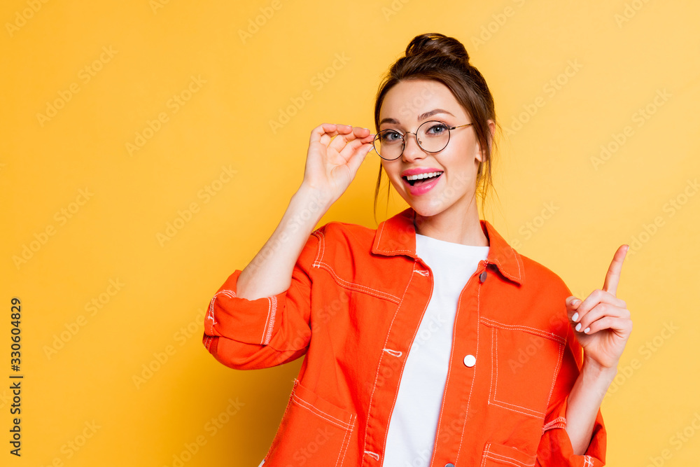 happy student touching eyeglasses and showing idea gesture while looking at camera on yellow background happy student touching eyeglasses and showing idea gesture while looking at camera on yellow background