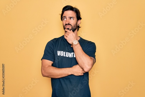 Young handsome hispanic volunteer man wearing volunteering t-shirt as social care Thinking worried about a question, concerned and nervous with hand on chin