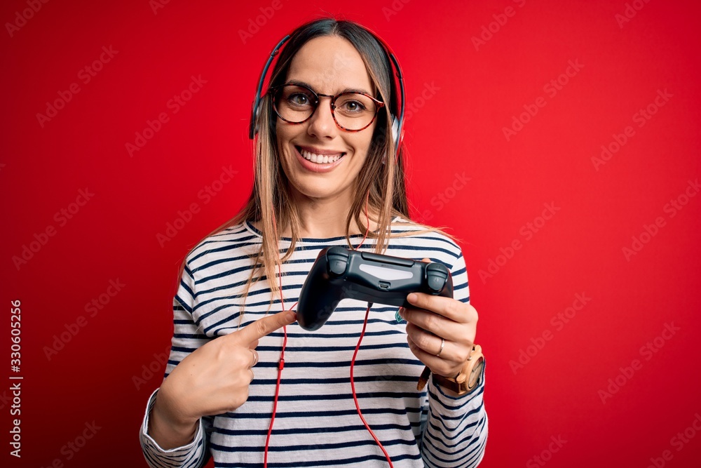 Young blonde gamer woman using gamepad playing video games over red background very happy pointing with hand and finger Young blonde gamer woman using gamepad playing video games over red background very happy pointing with hand and finger