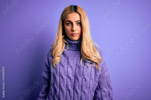 Young beautiful blonde woman wearing casual turtleneck sweater over purple background Relaxed with serious expression on face. Simple and natural looking at the camera.