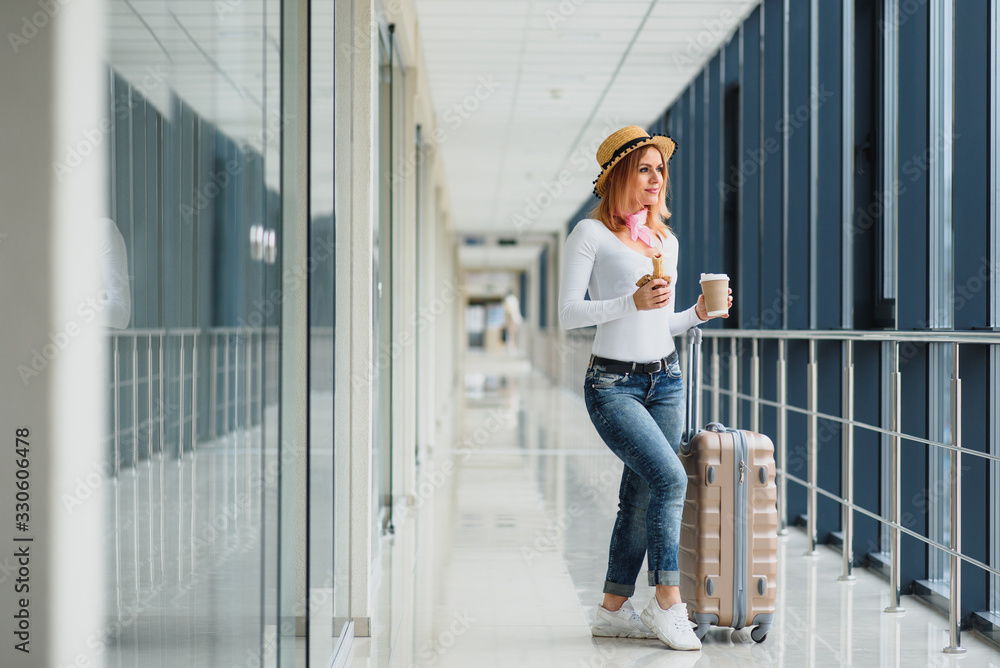 Portrait of successful business woman traveling with case at airport. Beautiful stylish female travel with luggage. Woman waiting for plane and drinking coffee