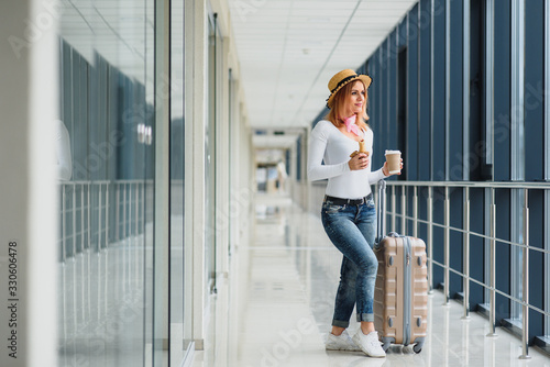 Portrait of successful business woman traveling with case at airport. Beautiful stylish female travel with luggage. Woman waiting for plane and drinking coffee