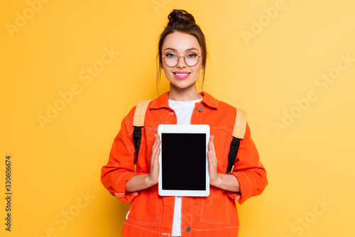 smiling student in eyeglasses showing digital tablet with blank screen on yellow background photo