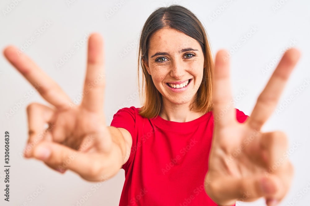 Beautiful redhead woman wearing casual red t-shirt over isolated background smiling looking to the camera showing fingers doing victory sign. Number two. Beautiful redhead woman wearing casual red t-shirt over isolated background smiling looking to the camera showing fingers doing victory sign. Number two.