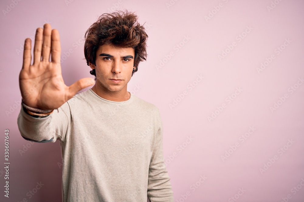 Young handsome man wearing casual t-shirt standing over isolated pink background doing stop sing with palm of the hand. Warning expression with negative and serious gesture on the face. Young handsome man wearing casual t-shirt standing over isolated pink background doing stop sing with palm of the hand. Warning expression with negative and serious gesture on the face.