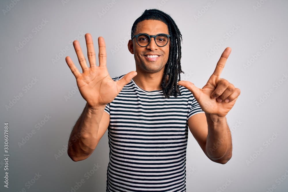 Young handsome african american man with dreadlocks wearing striped t-shirt and glasses showing and pointing up with fingers number seven while smiling confident and happy. Young handsome african american man with dreadlocks wearing striped t-shirt and glasses showing and pointing up with fingers number seven while smiling confident and happy.
