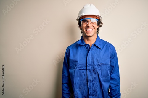 Young constructor man wearing uniform and security helmet over isolated white background with a happy and cool smile on face. Lucky person.