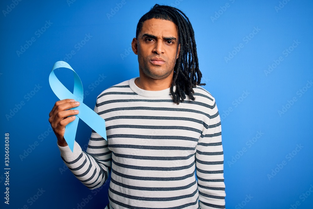 Young african american afro man with dreadlocks holding blue cancer ribbon with a confident expression on smart face thinking serious Young african american afro man with dreadlocks holding blue cancer ribbon with a confident expression on smart face thinking serious