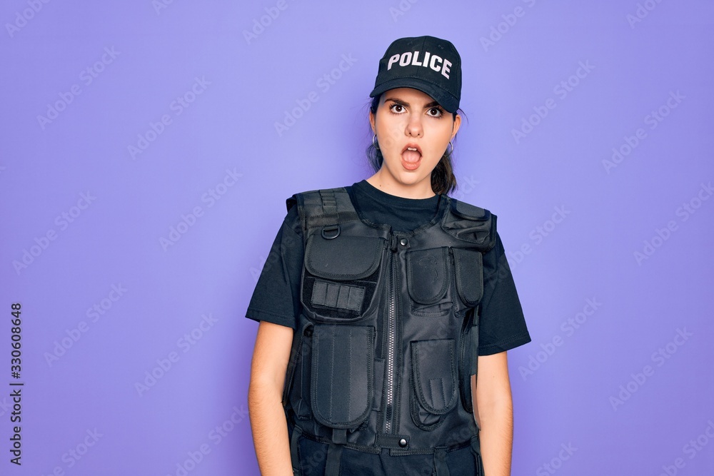 Young police woman wearing security bulletproof vest uniform over purple background In shock face, looking skeptical and sarcastic, surprised with open mouth Young police woman wearing security bulletproof vest uniform over purple background In shock face, looking skeptical and sarcastic, surprised with open mouth
