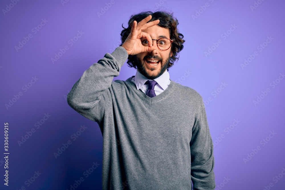 Handsome businessman with beard wearing tie and glasses standing over purple background doing ok gesture with hand smiling, eye looking through fingers with happy face. Handsome businessman with beard wearing tie and glasses standing over purple background doing ok gesture with hand smiling, eye looking through fingers with happy face.