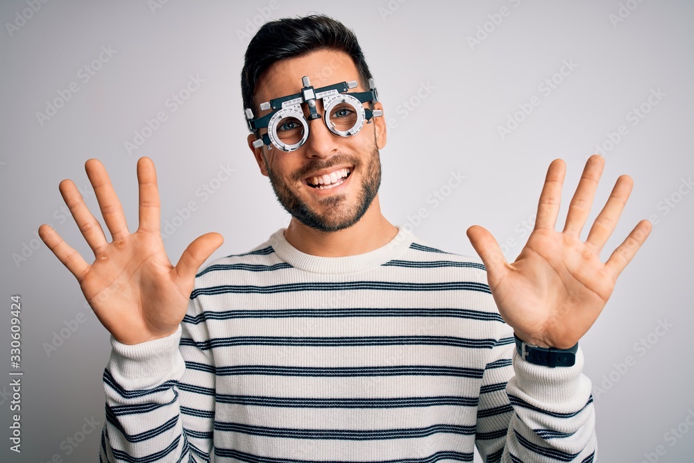 Naklejka premium Young handsome man with beard wearing optometry glasses over isolated white background showing and pointing up with fingers number ten while smiling confident and happy.