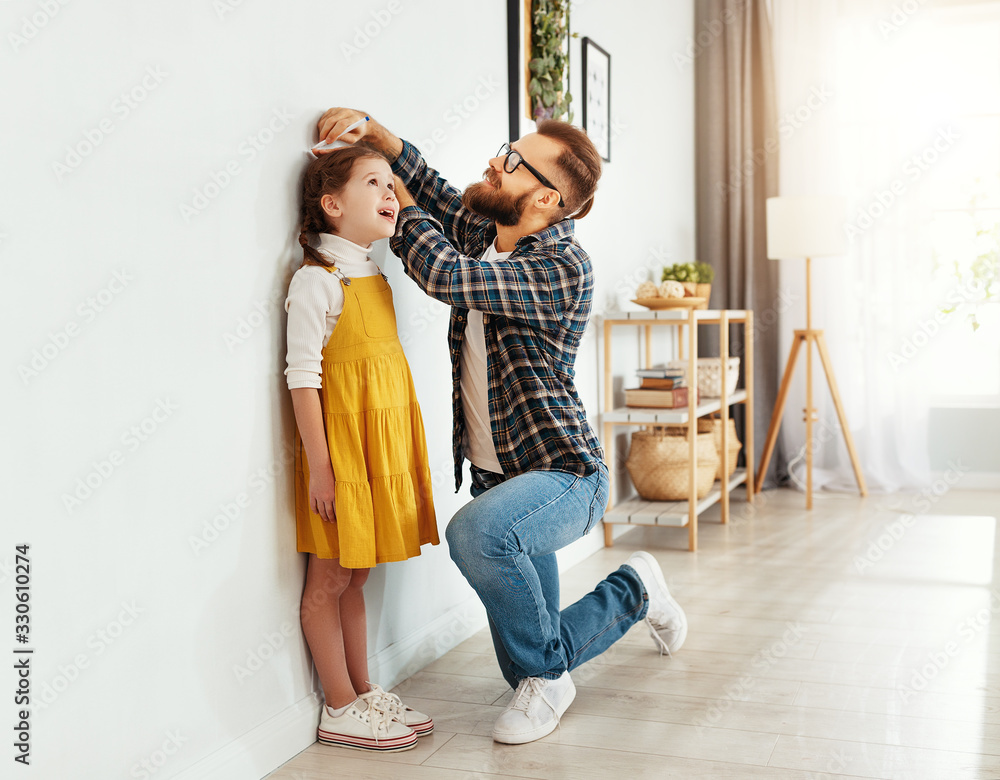 father measuring height of daughter at home. - obrazy, fototapety, plakaty 