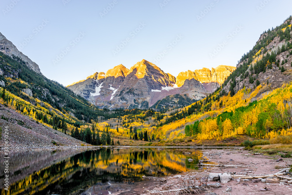 Maroon Bells lake at sunrise sunlight in Aspen, Colorado with rocky mountain peak and snow in October 2019 autumn and vibrant trees reflection on water