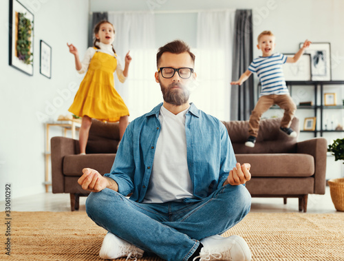 Father meditating in room with playful kids photo