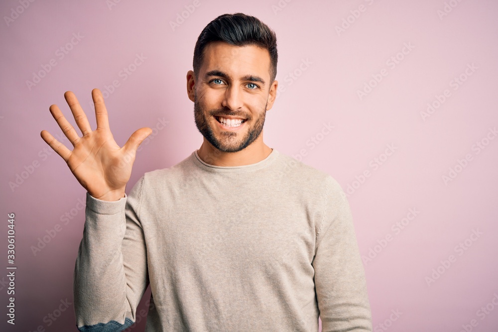 Young handsome man wearing casual sweater standing over isolated pink background showing and pointing up with fingers number five while smiling confident and happy. Young handsome man wearing casual sweater standing over isolated pink background showing and pointing up with fingers number five while smiling confident and happy.