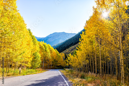 Sunburst through forest in Aspen, Colorado maroon bells mountains in October 2019 and vibrant trees foliage autumn and sky along road photo