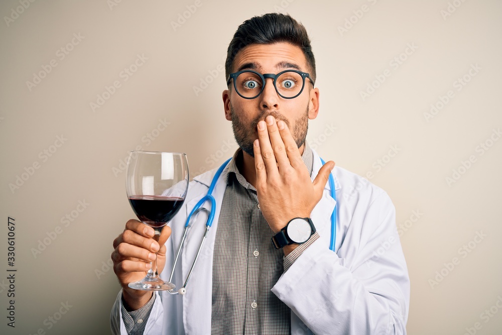 Young doctor man wearing stethoscope drinking a glass of fresh wine over isolated background cover mouth with hand shocked with shame for mistake, expression of fear, scared in silence, secret concept Young doctor man wearing stethoscope drinking a glass of fresh wine over isolated background cover mouth with hand shocked with shame for mistake, expression of fear, scared in silence, secret concept