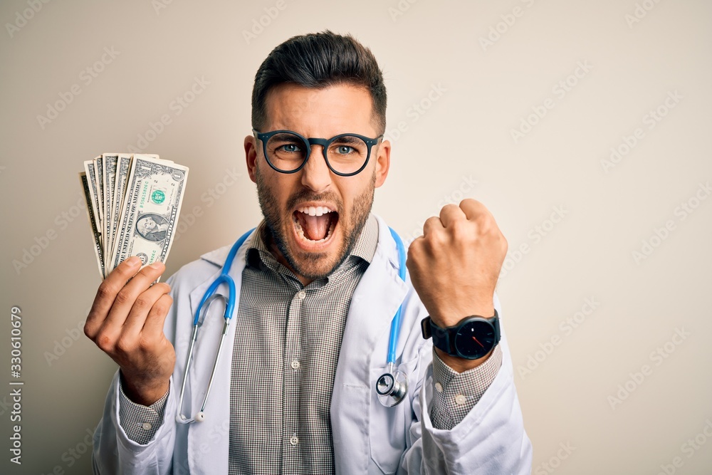 Young doctor man holding a bunch of one dollar banknotes over isolated background annoyed and frustrated shouting with anger, crazy and yelling with raised hand, anger concept Young doctor man holding a bunch of one dollar banknotes over isolated background annoyed and frustrated shouting with anger, crazy and yelling with raised hand, anger concept